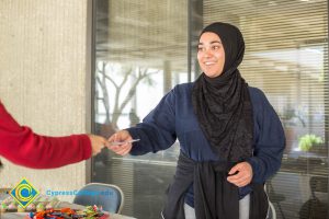 A woman wearing a hijab handing a paper to someone.