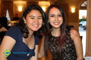 Female student in navy blue dress next to female student in black lace dress, smiling