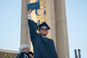 Young man in cap and gown holding degree and raising his hands