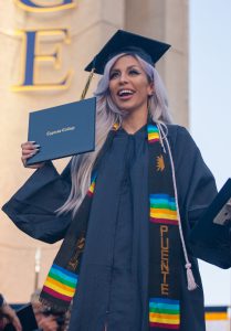 Female student wearing cap and gown and Puente sash, smiling and holding her degree