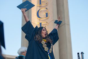 Girl in cap and gown holding degeee and raising her hands