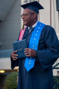 Male student wearing cap and gown holding degree