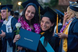 Two female students smiling and holding Cypress College degree and white rose