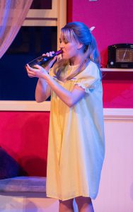 Young blonde woman with a bottle of wine, performing a scene from Grease.