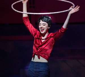 Theater student in a red shiny blouse holding a hula hoop in a scene from Grease.