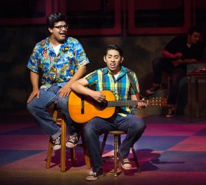 Two male students, one playing a guitar, performing a scene from Grease.