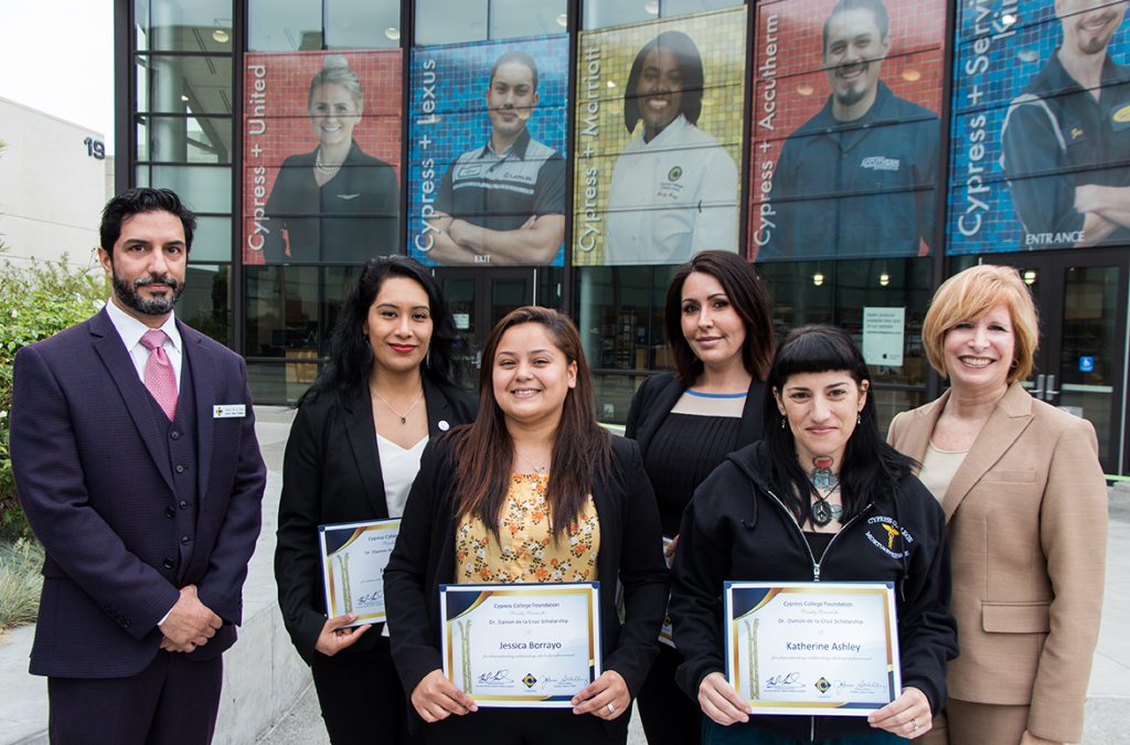 College President and Professor standing with students holding scholarships in front of bookstore