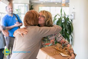 Gail Taylor hugging President, JoAnna Schilling with Marc Posner looking on in the background.