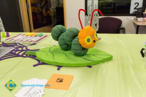 Mini pumpkins painted green to look like caterpillar body with mini orange pumpkin face sitting on a painted green leaf