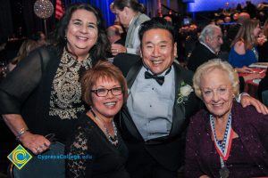 A smiling man in a tuxedo and three women smiling at the 2018 Americana Awards.