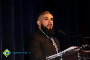 A young man with shaved head and beard and moustache at the microphone.