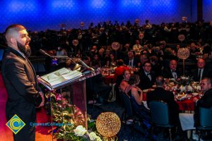 Audience at banquet tables watching a speaker at the 2018 Americana Awards.