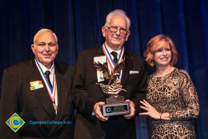 Dr. JoAnna Schilling with two men in suits and tie wearing award medals. One man is holding a Man of the Year award.