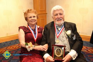 Man and woman wearing award medals and holding an award clock.