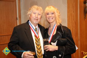 A woman with blonde hair holding a glass and a man in a suit and colorful tie smiling.