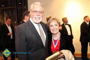 A man in glasses with grey hair, moustache and beard and a woman with short blonde hair wearing a medal around her neck.