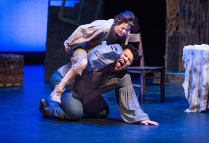 Male student on the kneeling on the ground on stage, with female student on top of him during a performance of Oliver Twist