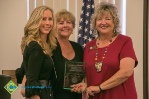 Three women smiling and holding an award.