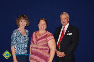 A woman in a pink stripped shirt with a woman in a blue print shirt and a gentleman in a black suit and red tie.