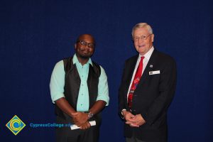 Scholarship recipient with glasses and teal shirt and black vest with a man in a black suit and red tie.