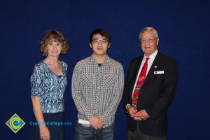 A young man in a checkered shirt and glasses with a woman in a blue print shirt and a gentleman in a black suit and red tie.