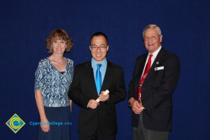 A young man in a black suit , blue shirt and tie with a woman in a blue print shirt and a gentleman in a black suit and red tie.