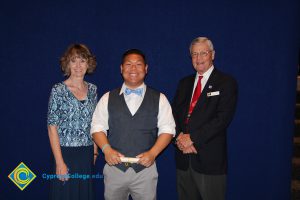 A young man in a grey vest, white shirt and blue bowtie with a woman in a blue print shirt and a gentleman in a black suit and red tie.