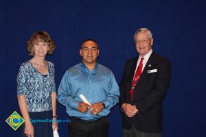 A young man in a blue shirt with a woman in a blue print shirt and a gentleman in a black suit and red tie.