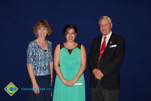 A young woman in a teal and black dress with a woman in a blue print shirt and a gentleman in a black suit and red tie.