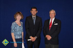 A young man in a black suit and tie with a woman in a blue print shirt and a gentleman in a black suit and red tie.