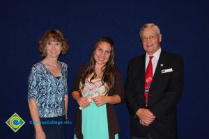 Student showing her scholarship award with a woman in a blue print shirt and a gentleman in a black suit and red tie.