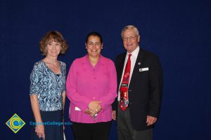 A young woman in a pink blouse with a woman in a blue print shirt and a gentleman in a black suit and red tie.