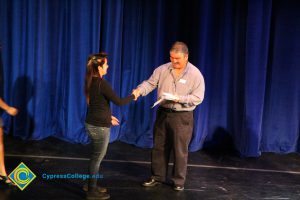 David Okawa shaking hands with a young lady in a black shirt and blue jeans.