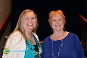 A woman in a teal and black blouse with white sweater and a woman in a blue blouse smiling.