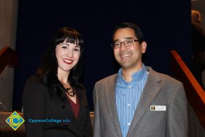 A young lady with black hair and black blazer with a young man in grey jacket and blue stripped shirt.