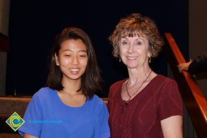 A woman with short brown hair and a red sweater standing with a young lady in a blue shirt and short brown hair.