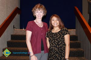 A woman with short brown hair and a red sweater standing with a young lady in a black dress and short brown hair.