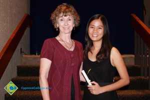 A woman with short brown hair and a red sweater standing with a young lady in a black dress and long brown hair.