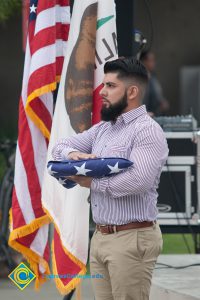 Bearded young man holding folded American flag.