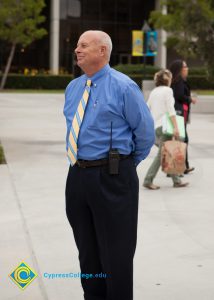 A man in a blue dress shirt and tie standing on campus.