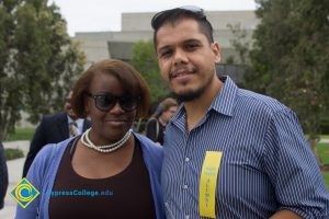 A man in a blue shirt standing with a woman in a black shirt and blue sweater.