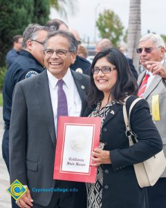 A man in a suit and tie and a woman with black hair ad black sweater smiling.