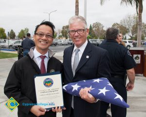 Bob Simpson holding folded American flag with a gentleman in a white shirt and tie holding a certificate.