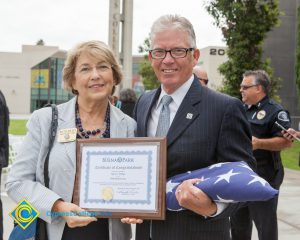 Bob Simpson holding folded flag with a woman holding a Certificate of Congratulations.