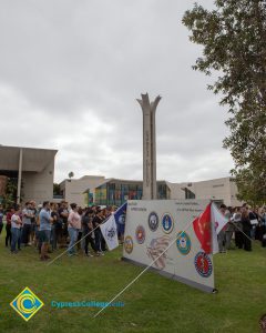 Banner with campanile in the background with a crowd of people on the lawn.