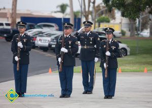 Military personnel in uniform, holding rifles.