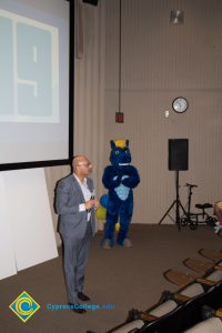 Peter Maharaj speaking at the Ideathon event with Charlie the Charger looking on.