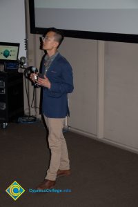 Man in a blue coat and tan pants speaking to an audience.