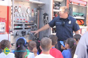 A firefighter showing young children the parts of the fire truck.