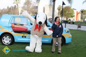 Snoopy standing with a young lady in tan khaki pants and a blue jacket.